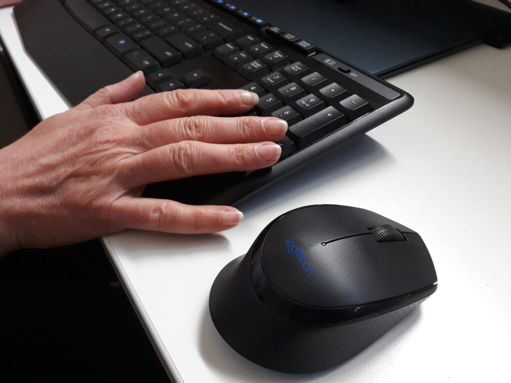 Close up of a hand resting on a computer keyboard. There is a mouse beside the keyboard.